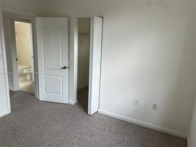 Neutral-toned wall-to-wall carpeting, white interior doors with brass-finish hardware, and built-in closet storage