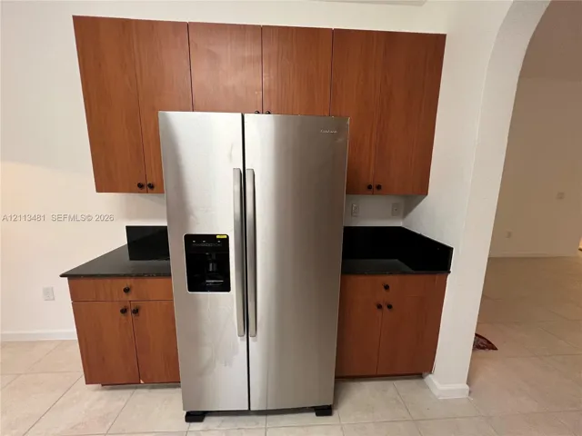 Kitchen cabinetry with wood-finish flat-panel doors, dark stone-surface countertops, and a side-by-side stainless steel refrigerator