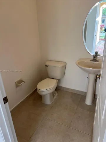 Powder room featuring tile flooring, pedestal sink, oval wall-mounted mirror, and standard-height toilet
