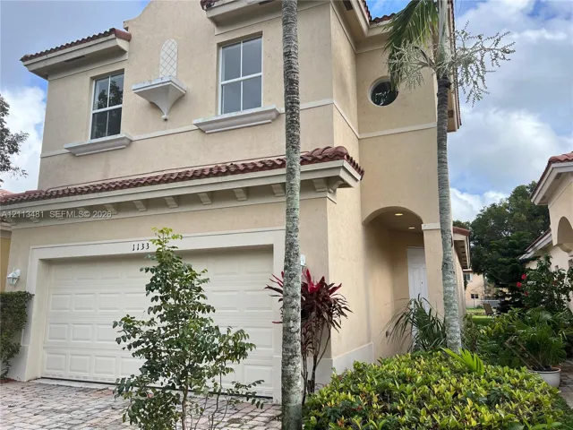 Stucco exterior featuring mission-style roof tiles, an arched entryway, decorative corbel details, and a paved driveway