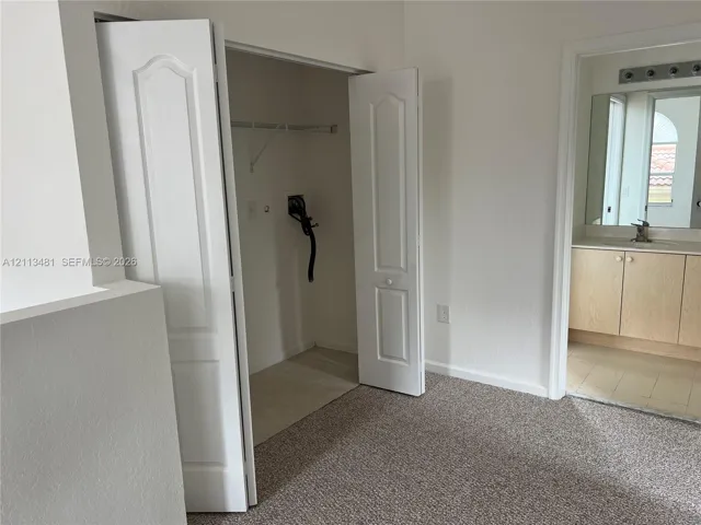 Carpeted room featuring a closet with bi-fold doors and built-in shelving, plus a bathroom with wood-finish cabinetry and a framed mirror