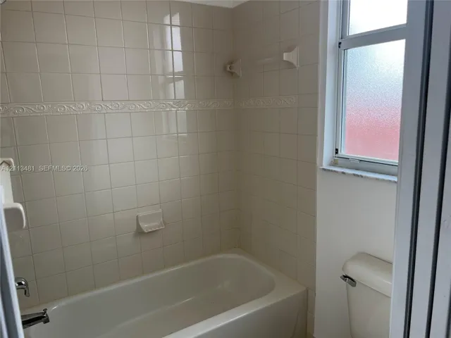 Bathtub with a built-in soap dish and decorative tile surround, completed by a window with privacy glass and a two-piece toilet