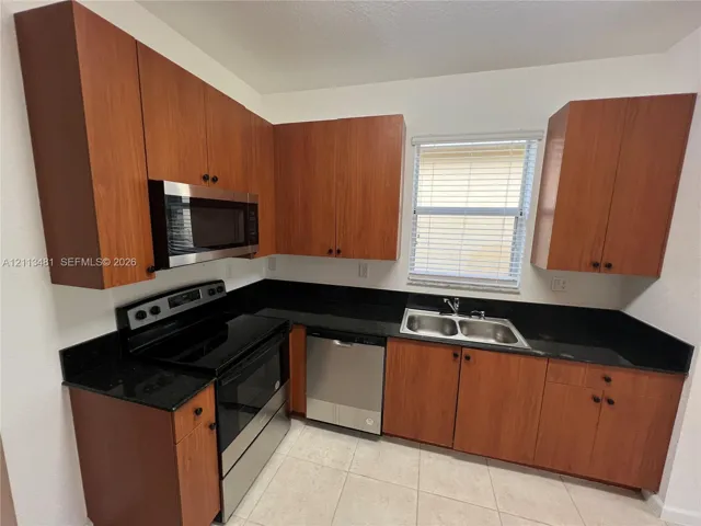 Kitchen featuring wood-finish cabinetry, dark solid-surface countertops, stainless steel appliances, double-basin sink, and ceramic tile flooring