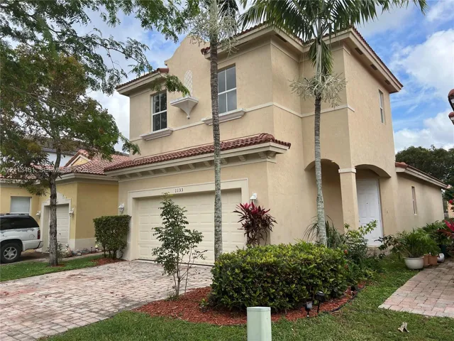Two-story stucco exterior featuring a tiled roof, arched entryway, brick-paver driveway, and decorative architectural detailing
