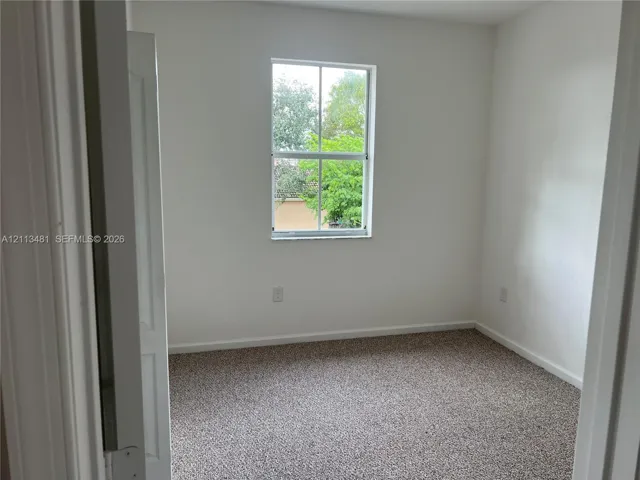 Neutral-toned room with wall-to-wall carpeting, crisp white walls, and a single-hung window featuring a mullion