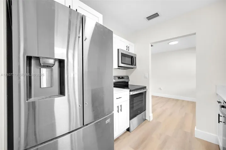 Kitchen featuring white cabinetry with matte black hardware, stainless steel refrigerator with external water dispenser, stainless steel microwave, stainless steel range, and wood-finish flooring