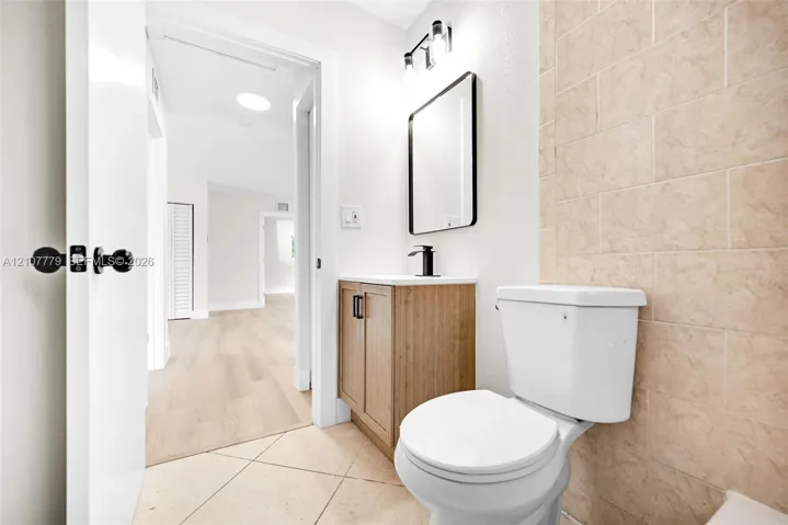 Bathroom featuring a wood-finish vanity with a white countertop, matte black faucet, framed mirror, and tile wall accents
