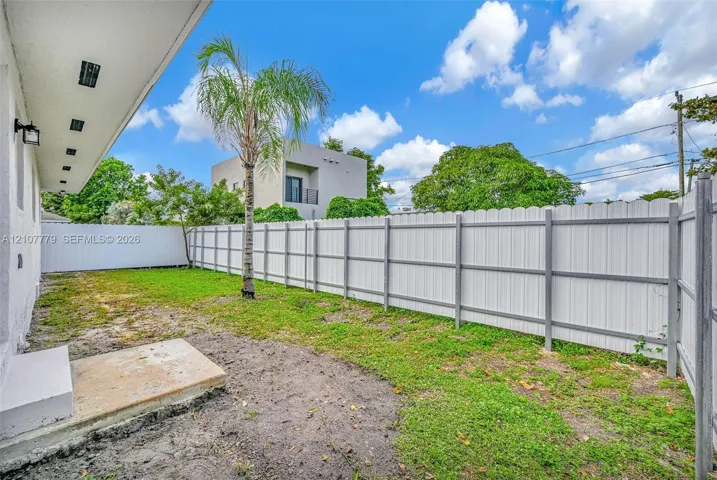 Fenced backyard featuring a concrete patio, lawn area, and a mature palm tree