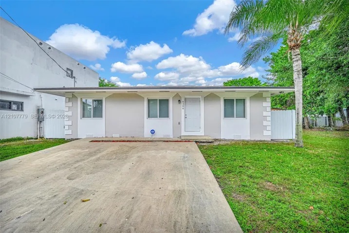 Single-story exterior featuring a light-toned smooth finish, quoined corner detailing, a central entry door, and a concrete driveway
