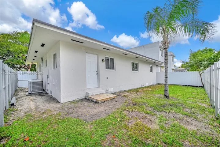 Stucco exterior featuring a low-slope roof, white vinyl fencing, and a mature palm tree