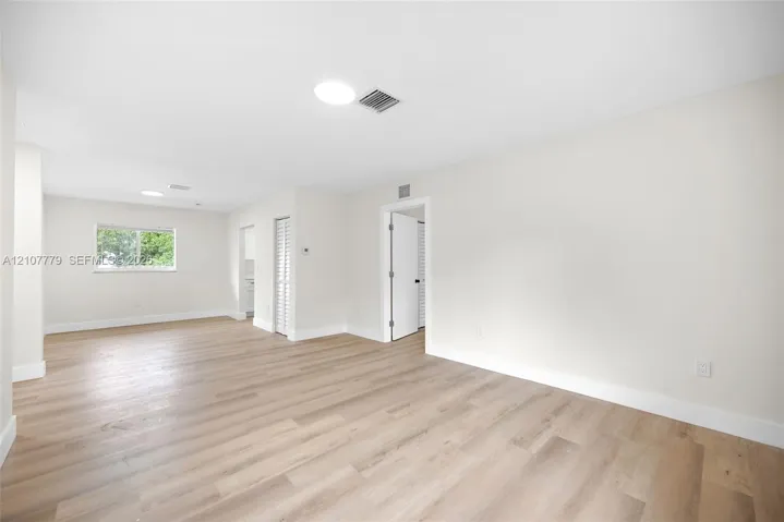 Open-concept interior space featuring light-toned wood-finish flooring, recessed circular lighting, a window with exterior exposure, and white louvered closet doors