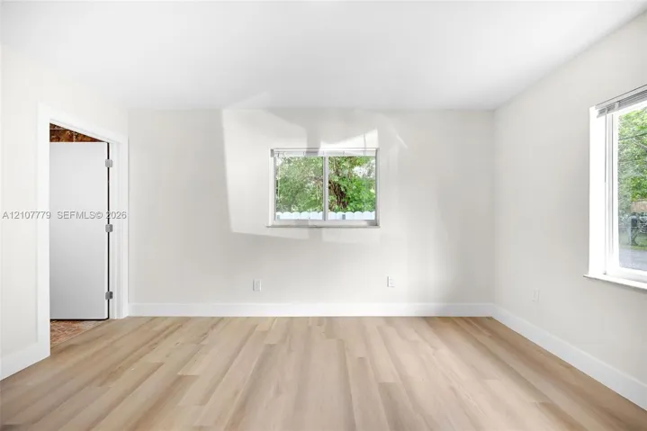 Neutral-toned interior room featuring wood-finish flooring, two sliding windows, and a doorway with a neutral-finished door
