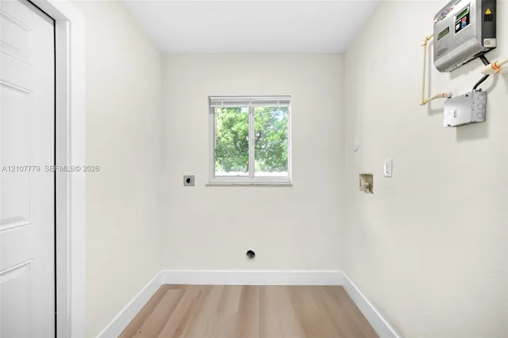 Neutral-toned space featuring wood-finish flooring, a centrally located single-pane window, and utility hookups