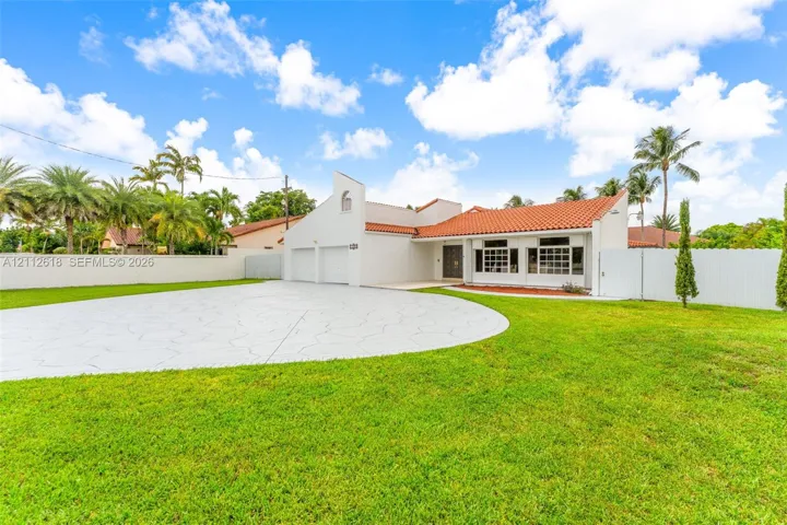 Stucco exterior featuring a terracotta tile roof, two-car garage, patterned concrete driveway, and expansive fenced yard