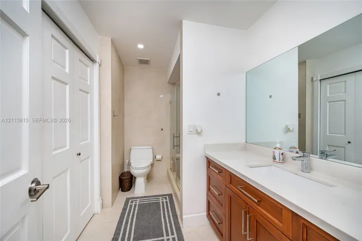 Bathroom featuring a wood-finish vanity with a stone-composite countertop, an integrated rectangular sink, a full-width wall mirror, and a glass-enclosed shower