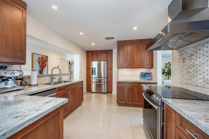 Kitchen featuring wood cabinetry, stone countertops, stainless steel appliances, a decorative tile backsplash, and tile flooring