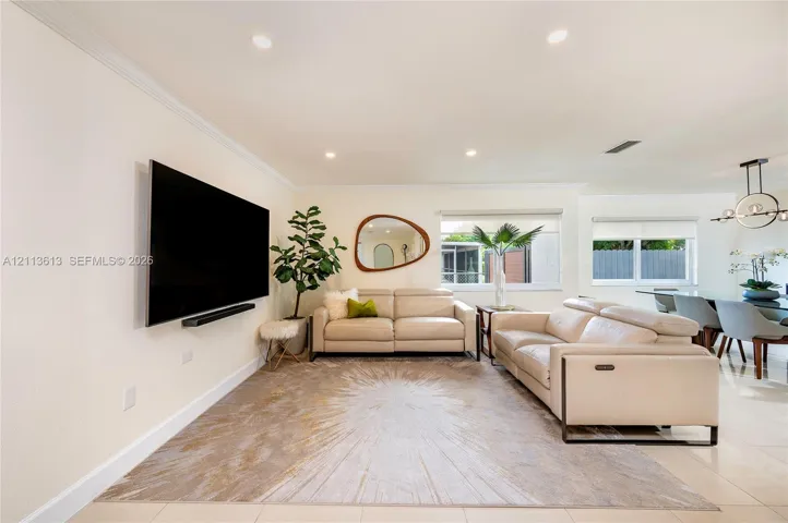 Living area featuring large format tile flooring, recessed lighting, crown molding, and dual windows with roller shades