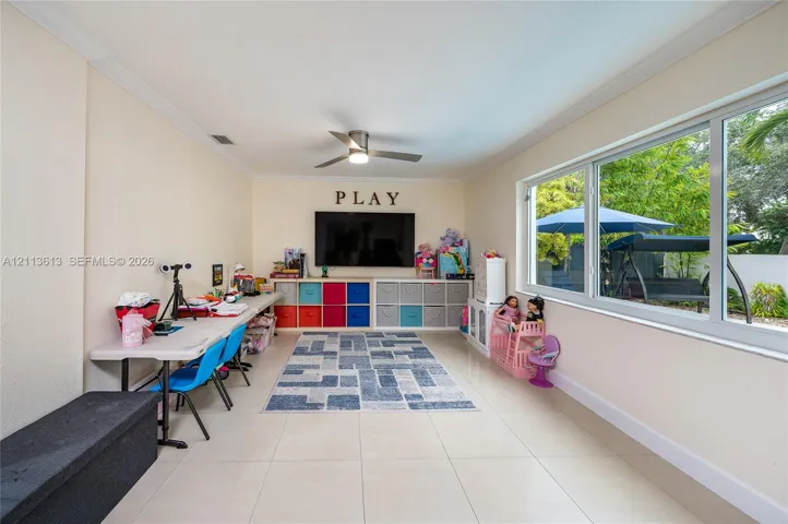 Spacious room featuring large format neutral tile flooring, expansive windows, crown molding, and a modern ceiling fan