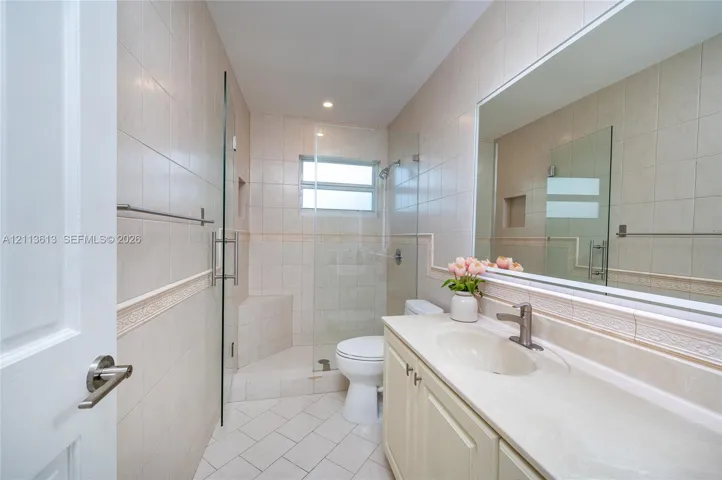 Bathroom featuring a vanity with a solid-surface countertop, an integrated sink, and brushed-finish faucet, along with a walk-in shower with a glass enclosure, built-in shelving, and floor-to-ceiling wall tile