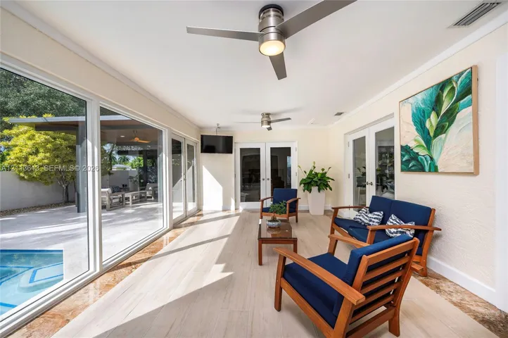 Sunroom featuring neutral tile flooring, dual ceiling fans, expansive floor-to-ceiling glass sliding doors, and double glass-pane entry doors