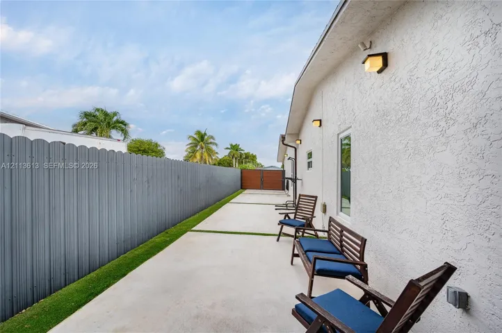 Side yard featuring a concrete patio with grass inlays, a full-height corrugated metal privacy fence, wood-tone double gate, and exterior wall-mounted lighting fixtures