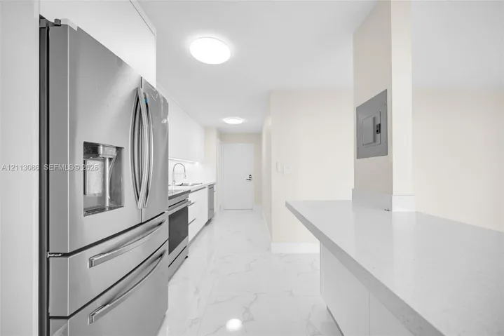 Kitchen featuring stainless steel refrigerator, white cabinetry, solid-surface countertops, and stone-finish tile flooring