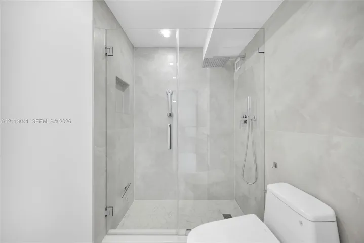 Walk-in shower featuring a frameless glass enclosure, floor-to-ceiling large-format tile surround, integrated shower niche, and wall-mounted shower system