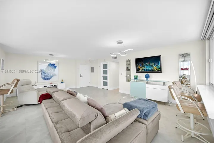 Open-concept living space featuring large-format tile flooring, recessed lighting, modern sculptural light fixtures, and a glass-paneled interior door