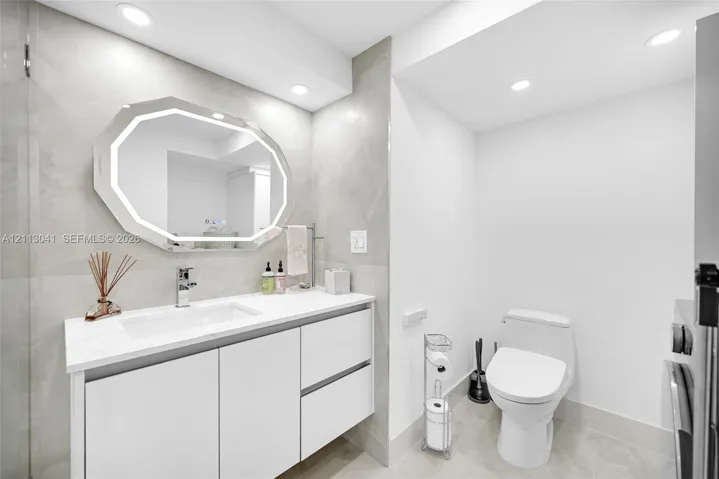Modern floating vanity featuring white cabinetry, a rectangular sink, and a light-toned countertop, paired with an octagonal LED-backlit mirror and large-format wall tile