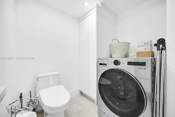 Compact room featuring a floor-to-ceiling white storage cabinet, a sleek one-piece toilet, and tile flooring