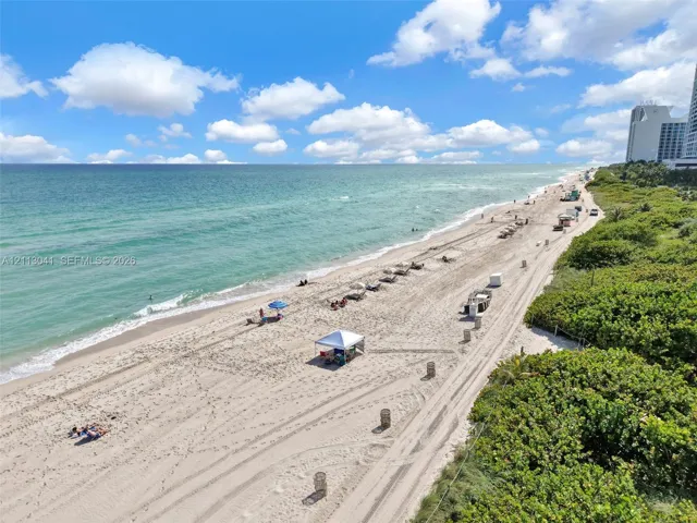 Direct oceanfront access featuring expansive sandy shoreline, turquoise water, and mature coastal vegetation