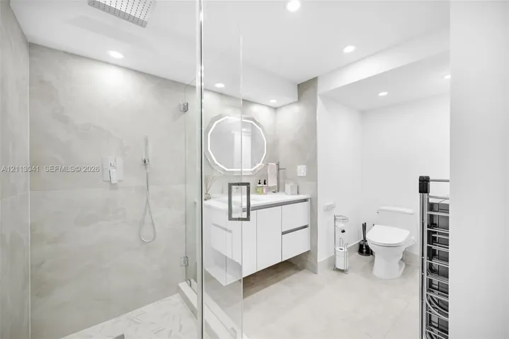 Walk-in shower with floor-to-ceiling stone-finish tile, rainfall shower head, glass enclosure, floating vanity, and recessed lighting