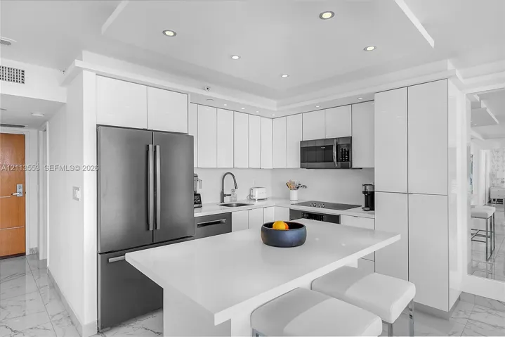Kitchen featuring high-gloss white cabinetry, white stone countertops, an oversized center island, stainless steel appliances, and recessed ceiling lighting