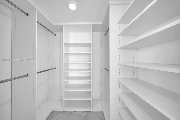 Custom walk-in closet featuring white built-in shelving, adjustable storage racks, metal garment rods, and stone-finish flooring