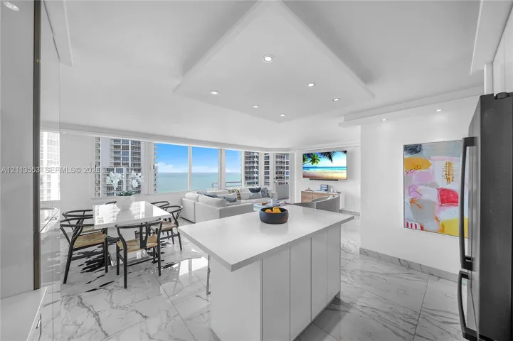 Open-concept space featuring expansive floor-to-ceiling windows, white cabinetry, a center island with a stone-finish countertop, and polished flooring with a marble-style pattern