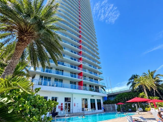 High-rise exterior featuring glass balcony railings, prominent structural red detailing, and an integrated swimming pool with surrounding terrace