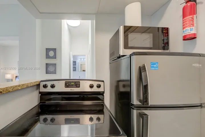 Stainless steel refrigerator, built-in microwave, and electric range with a glass cooktop, finished with a stone-surface pass-through counter