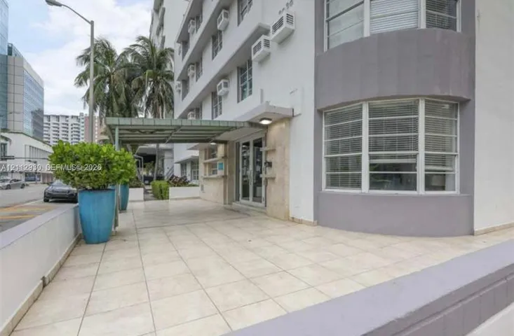 Exterior entrance featuring a covered porte-cochère, light-toned ceramic tile flooring, a glass-paneled entry door, and bay-style windows