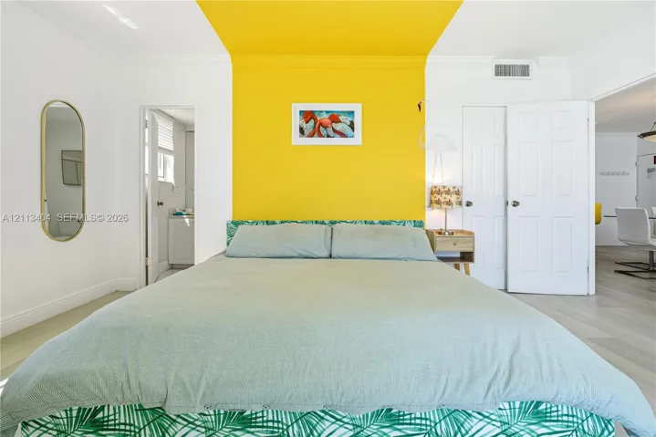 Room featuring wood-finish flooring, a wall-to-ceiling yellow accent, crown molding, and a tall oval wall-mounted mirror