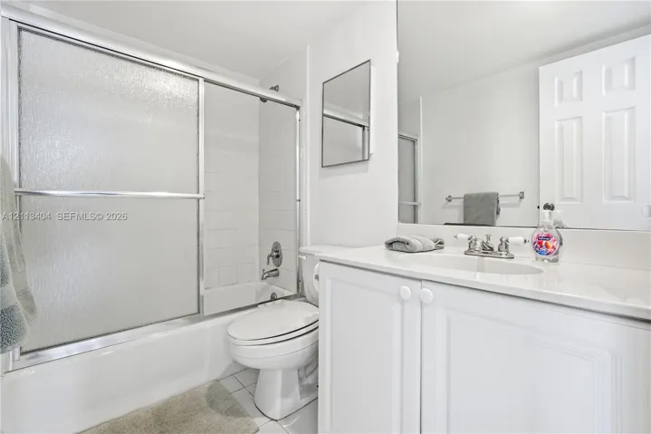 Bathroom featuring a white vanity cabinet with a stone-top integrated sink, chrome dual-handle faucet, oversized wall-mounted mirror, and a shower-tub combination enclosed by sliding glass doors