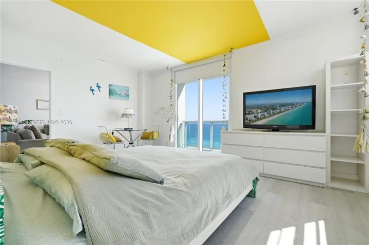 Full-height sliding glass doors with direct ocean access, integrated white built-in shelving, wood-finish flooring, and recessed ceiling feature