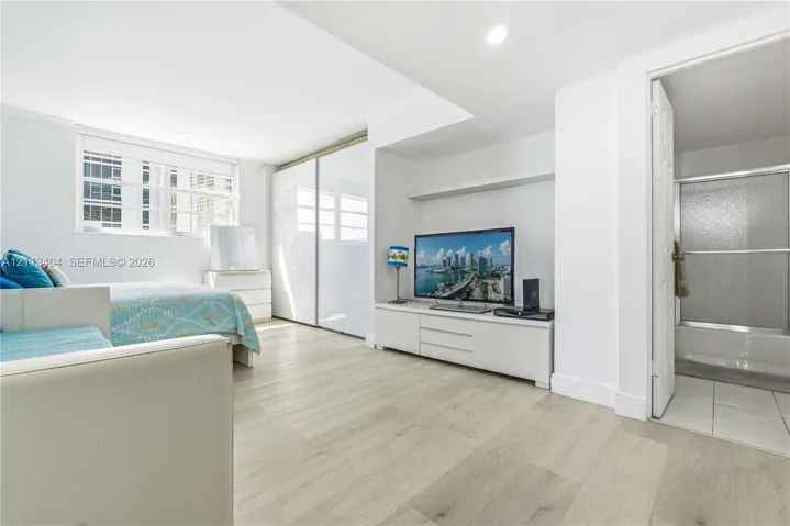 Light-filled room featuring wood-finish flooring, sliding-door closets with high-gloss panels, recessed lighting, and a bathroom containing a shower-tub combination