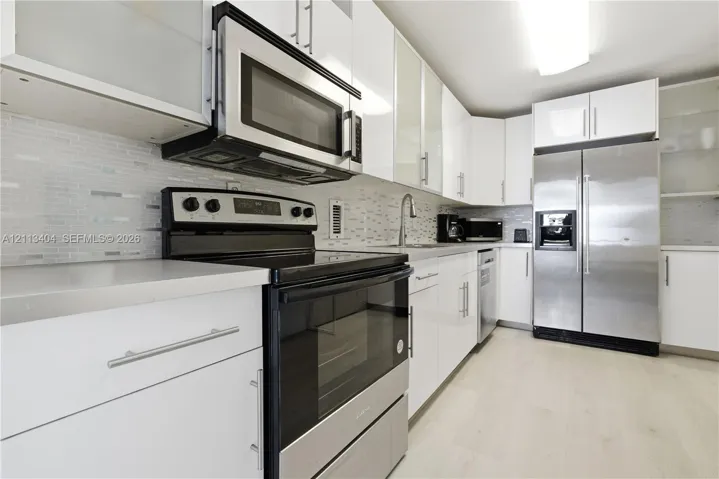 Kitchen featuring high-gloss white cabinetry, stainless steel appliances, light-toned hard-surface flooring, and a linear tile backsplash