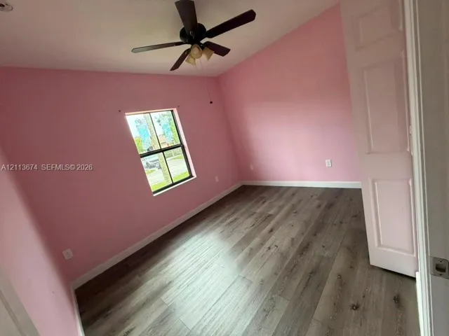 Room featuring wood-finish flooring, vaulted ceilings, a ceiling fan with integrated lighting, and a single-pane window