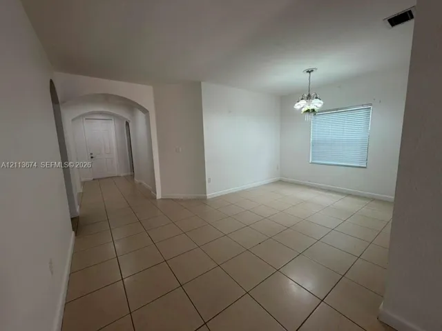 Interior space featuring large-format tile flooring, arched entryways, a multi-paneled door, and a decorative multi-bulb chandelier