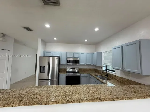 Kitchen featuring light blue cabinetry, stone-surface countertops, stainless steel appliances, dual-basin under-mount sink with matte black faucet, and recessed lighting