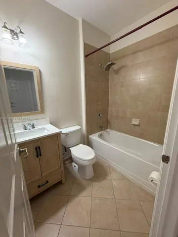 Bathroom featuring a wood-finish vanity with a rectangular sink, square tile flooring, a porcelain tub-and-shower combination with tiled surround, and a framed mirror