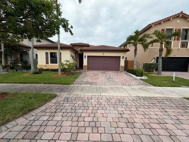 Single-story stucco exterior featuring a paver driveway, terracotta-style tile roof, integrated two-car garage, and shuttered window accents