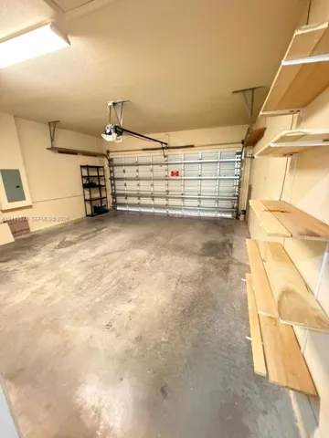 Two-car garage featuring a sectional metal door, concrete flooring, overhead lighting, and built-in wood shelving units