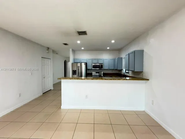 Kitchen featuring blue cabinetry, stone-finish countertops, stainless steel appliances, a breakfast bar, and tile flooring